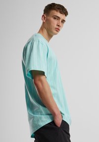 T-shirt court à manches courtes bleu sarcelle clair avec des rayures verticales blanches, présentant une coupe décontractée, un col en V et une texture en coton doux.