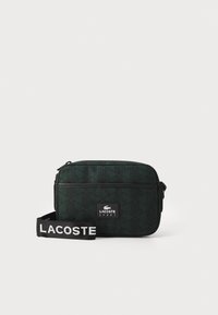 Borsa a spalla verde con un motivo a fantasia, di forma rettangolare, realizzata in tessuto testurizzato, con una cerniera nera e una tracolla staccabile con lettering bianco.