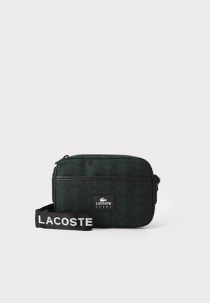 Borsa a spalla verde con un motivo a fantasia, di forma rettangolare, realizzata in tessuto testurizzato, con una cerniera nera e una tracolla staccabile con lettering bianco.