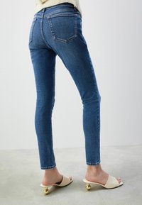 Smala blå jeans i denim, med medelhög midja, bakfickor och en ren finish. Kombinationen med slip-on sandaler med rundade guldfinish.