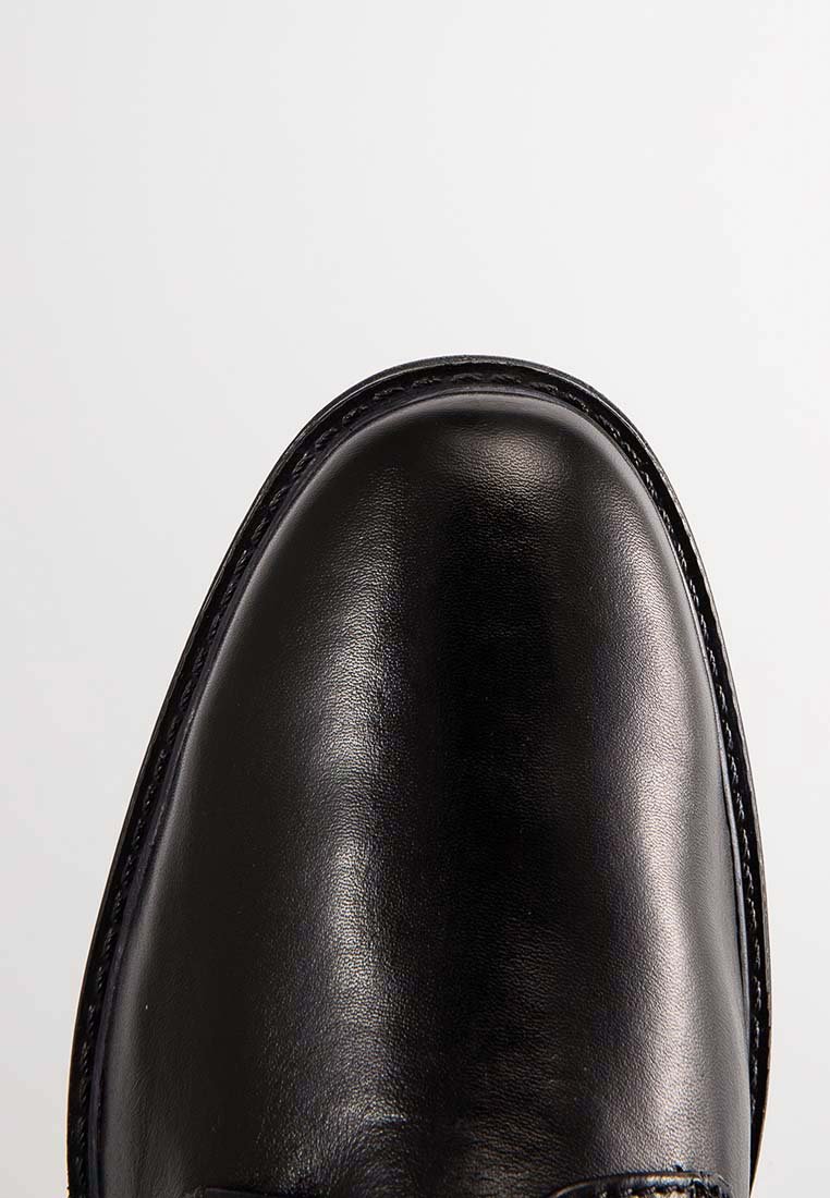Zwarte leren schoen met een glanzende afwerking. Rondneus, zichtbare stiksels en een lichte textuur. Minimalistisch ontwerp, gladde oppervlakte, zonder versieringen.