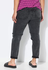 Jeans de mezclilla negra con corte ajustado, dobladillos en los extremos y dos bolsillos traseros, combinados con una blusa de patrón rosa brillante y sandalias negras de slide.