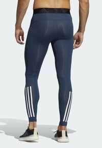 Granatowe legginsy sportowe z czarnym pasem w talii, na którym znajduje się logo Adidas, z trzema białymi paskami po bokach. Gładka tekstura.
