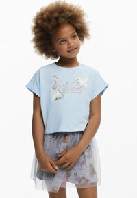 Lys blå cropped t-shirt med korte ærmer, med et grafisk design af kaniner og glimt; parret med en grå tylskørt med farverige mønstre.