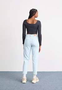 Black long-sleeve crop top, light blue high-waisted jeans, and beige sneakers with white socks. Rear view shows fitted design and casual style.