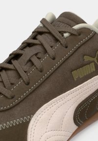 Zapatilla Puma de ante marrón con raya lateral beige, costuras detalladas, cordones marrones y logo de Puma visible en el lateral.