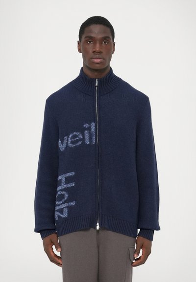 Maglione navy a zip con colletto alto, caratterizzato da motivi testuali blu chiaro e polsini e orlo a coste. Texture morbida e vestibilità rilassata.
