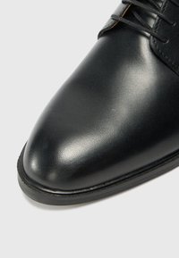 Zapato de vestir de cuero negro con un acabado suave, punta afilada y diseño de cordones. Cuenta con una suela resistente y acentos minimalistas.