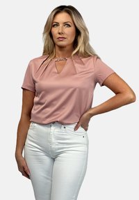 Blush pink short-sleeve top with a V-neck and pleated detailing at the shoulders, paired with white high-waisted jeans.