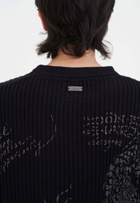 Maglione nero a coste con scollo rotondo, etichetta con logo metallico e sottili accenti a motivo di tono più chiaro.