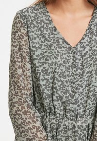 Šaty s leopardím potiskem v zelených a šedých odstínech, s rázem do V, předními knoflíky a elastickým pasem, s průhlednými dlouhými rukávy.