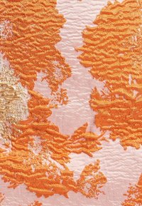 Broderie abstraite texturée orange sur un tissu rose clair, avec des motifs ondulés et des accents de fil beige brillant.