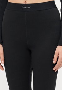Crne rebraste tajice s glatkim elastičnim pojasom i suptilnim Calvin Klein logom. Tkanina ima mekanu teksturu.