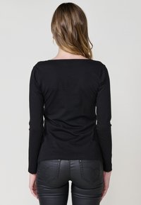 Haut noir à manches longues en tissu doux avec un col arrondi, associé à un pantalon en simili cuir noir avec des poches arrière détaillées.