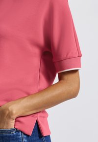 T-shirt rose à manches courtes avec une texture lisse, ourlet arrondi et accent blanc au poignet, avec une coupe décontractée. Associé à un denim.