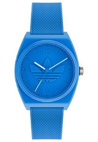Montre en silicone bleue avec un bracelet texturé. Cadran rond, logo en relief, index horaires en relief et aiguilles des heures et des minutes blanches.