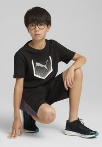 Camiseta negra de manga corta con un logotipo blanco de Puma, combinada con pantalones cortos negros y zapatillas deportivas negras con acentos en azul claro.