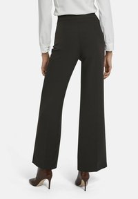 Zwarte wijde broek met een gladde textuur, hoge taille en een rechte snit. Draagt met bruine haklaarzen, wat een verzorgde uitstraling geeft.