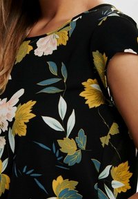 Haut en tissu noir avec des motifs floraux jaunes, roses et verts. Manches courtes avec une coupe décontractée et une texture lisse.