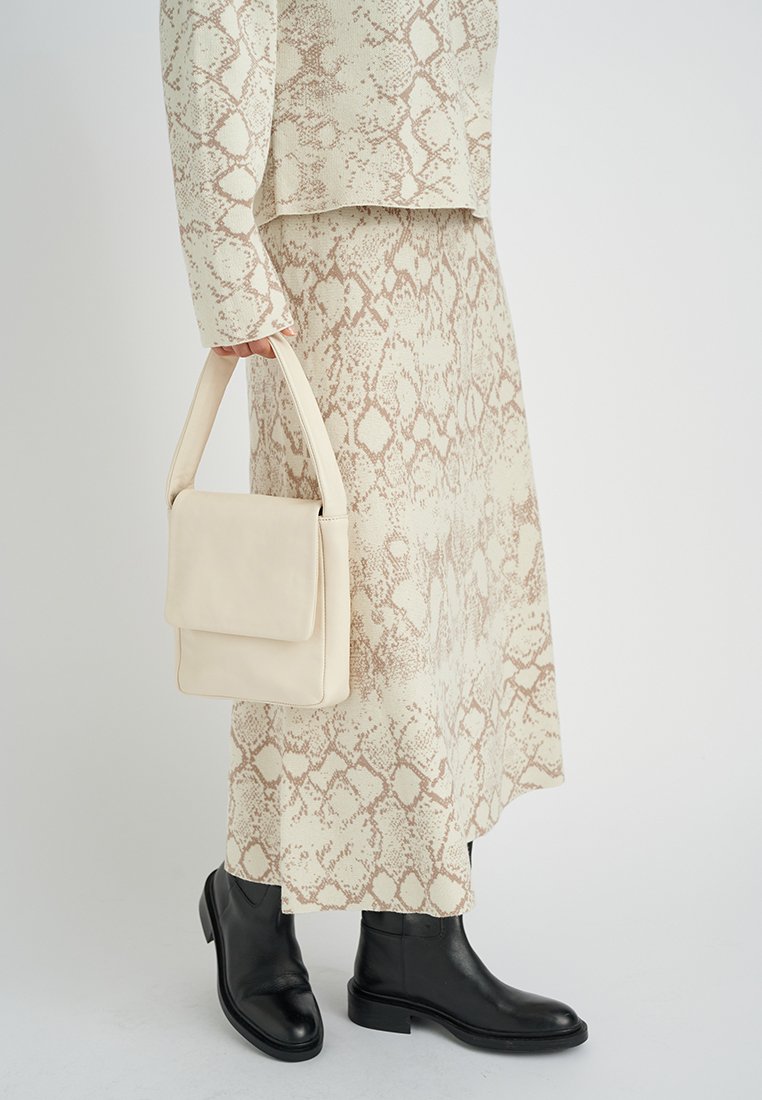 Cremige und beige Schlangenhautmuster-Outfit mit einem strukturierten, lockeren Oberteil, Rock und einer kleinen beigefarbenen Tasche; schwarze Knöchelstiefel.