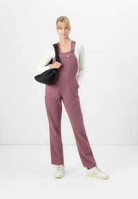Rosa corduroy overall med en avslappet passform, med justerbare stropper, metallspenner og lommer på siden, kombinert med en hvit langermet topp.