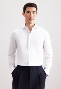 Witte langemanige dress shirt met een puntige kraag, met een gladde structuur en een sluiting met knopen aan de voorkant, gecombineerd met donkere geplooide broeken.