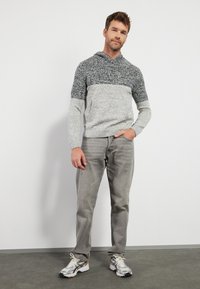 Felpa lavorata a maglia in grigio e blu navy con un motivo testurizzato, abbinata a jeans grigio chiaro e scarpe da ginnastica argento. Design leggero e informale.