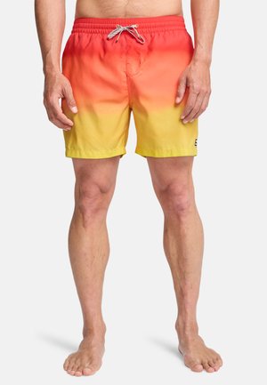 Model męski noszący kąpielówki ombre w kolorze czerwonym do żółtego z białym sznurkiem, stojący boso na białym tle.