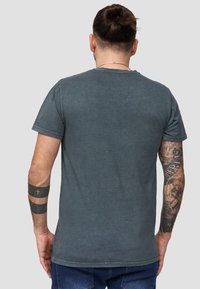 T-paita lyhyillä hihoilla, pyöreäkaula-aukko, tummanharmaasta puuvillasta, jossa on hieman haalistunut pinta ja suora helma, nähtynä takaa.