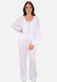 Weißes Zweiteiler-Outfit mit einem kurzärmeligen Oberteil und Spitzenakzenten sowie passenden hoch taillierten, weit geschnittenen Hosen. Weicher, strukturierter Stoff.