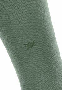 Primo piano di un tessuto di calzino verde con un sottile motivo floreale, che mette in evidenza la trama e le variazioni di colore.
