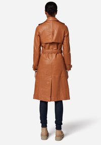 Tan leather trench coat with a belted waist, shoulder epaulets, and a tailored fit. Features a split back for added movement.