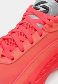 Φωτεινό ροζ αθλητικό παπούτσι με διχτυωτές πλαϊνές επιφάνειες, ζωηρές κορδόνες και γκρι γλώσσα με μαύρες λεπτομέρειες. Υλικά με υφή και κομψά στοιχεία σχεδίασης.