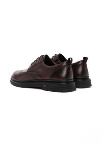 Zapatos de cuero marrón con diseño de punta alada, puntera redonda y suela de goma negra. Presentan perforaciones decorativas y una costura.