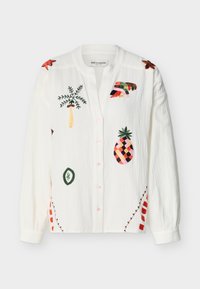 Chemise blanche à manches longues avec boutons et motifs tropicaux brodés colorés comprenant un ananas, un palmier et des formes abstraites.