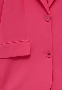 Blazer rose vif avec deux boutons assortis et une poche à rabat sur le côté avant gauche.