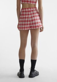 Røde og hvite rutete shorts med høy linning og glatt stoff, med en tettsittende design og rett snitt, kombinert med svarte sokker og sko.