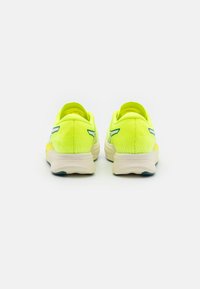 Žluté sportovní boty s texturovaným síťovým svrškem, zadním poutkem a kontrastní modrou podešví. Design se vyznačuje aerodynamickým tvarem.