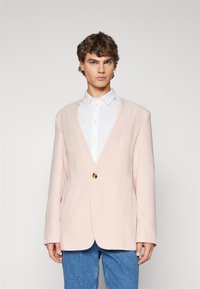 Staubrosa Blazer mit tiefem V-Ausschnitt, single goldener Knopfverschluss und langen Ärmeln, kombiniert mit einem weißen Hemd und Jeans.