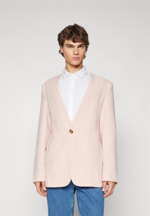 Dusty pink blazer with a deep V-neck, single gold button closure, and long sleeves, paired with a white shirt and denim pants.