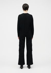 Camisola preta de malha com um design texturizado, combinada com calças cargo pretas acampanadas, com bolsos laterais e bainha ligeiramente aberta em boca de sino.