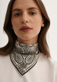 Czarnobiały szal w wzór paisley, wykonany z bawełny, w kształcie trójkąta, noszony na szyi, z napisem "LEBRAND" na dole.