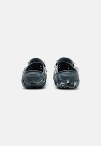 Black and white patterned clogs with a closed toe, back strap, and ventilation holes, made of lightweight material.