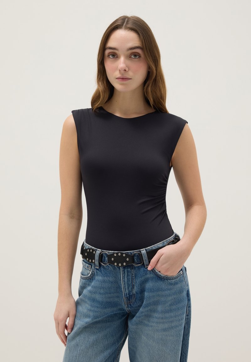 Body negro sin mangas con cuello redondo, diseño ajustado, combinado con jeans de mezclilla azul claro de talle alto y un cinturón negro con tachuelas.