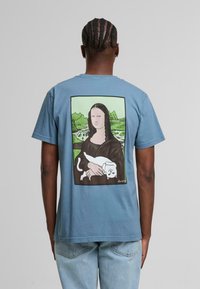 Kurze Ärmel blaues T-Shirt mit einem gedruckten Design auf der Rückseite, das eine Neuinterpretation der Mona Lisa zeigt, die eine weiße Katze hält.