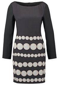 Robe noire cintrée à manches longues avec un col rond et des rangées horizontales de grands motifs circulaires blancs sur le devant.