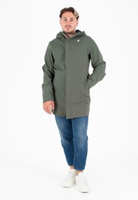 Cappotto impermeabile verde con zip frontale e chiusura a scatto. Presenta un cappuccio, tasche laterali e una texture liscia. Stile casual con denim.