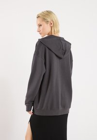 Hoodie u boji ugljena s opuštenim krojem, kapuljačom s vezicom i rukavima na manžetama, u kombinaciji s crnom suknjom koja ima bočni prorez.