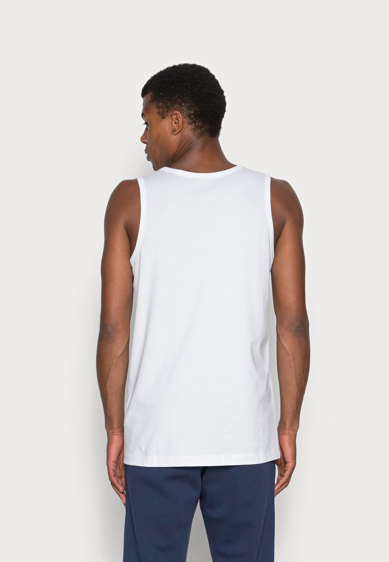 Débardeur en coton blanc avec un col rond et des bretelles larges, présentant une texture lisse et une coupe standard, porté avec un pantalon marine.
