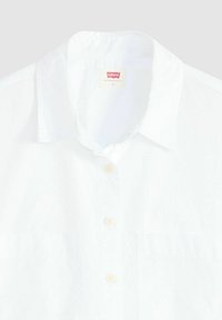 White button-up shirt with a classic collar. Made of lightweight fabric, features plain design and beige buttons. Includes a Levi's label.